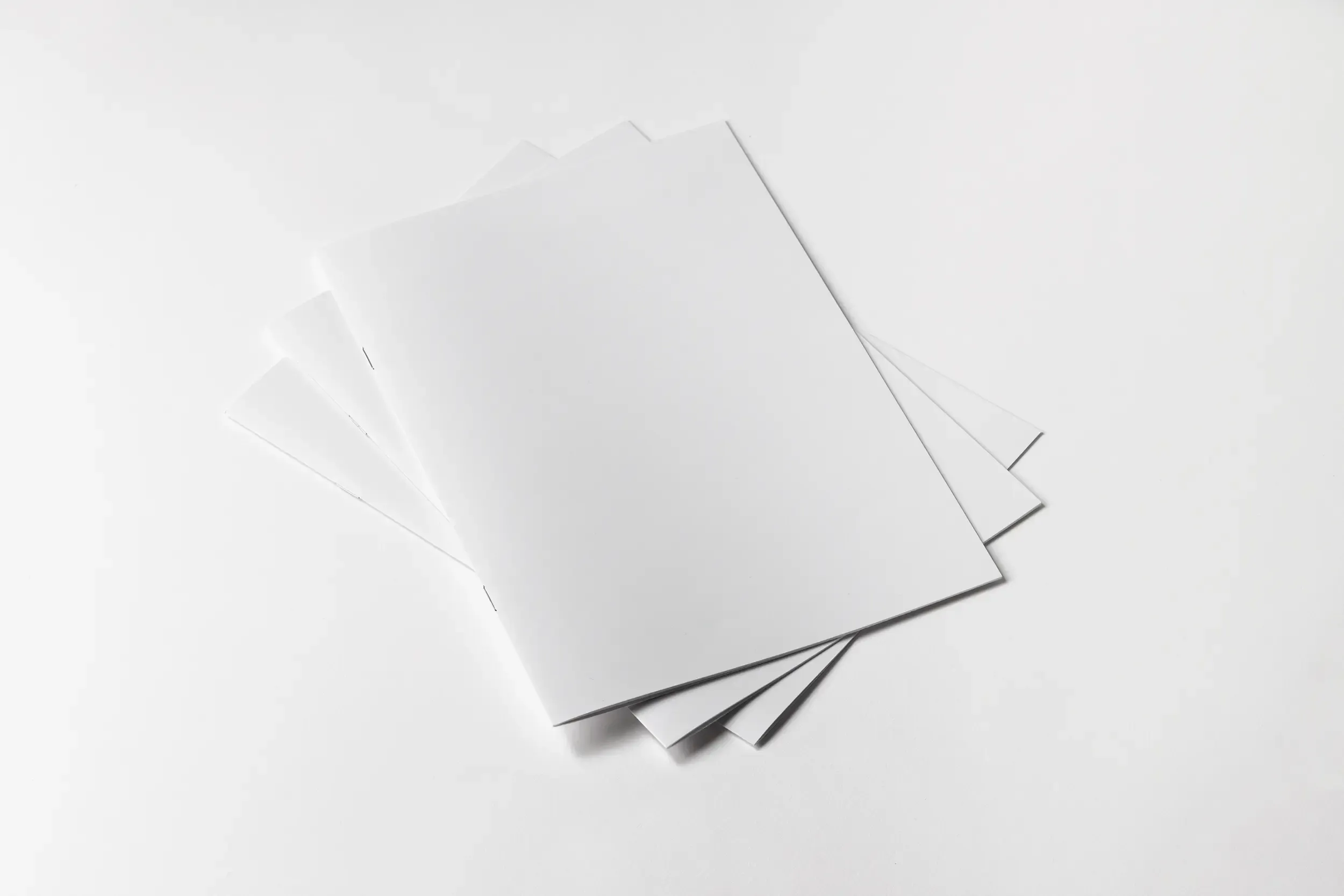 Gazetka reklamowa szyta złożona z kilku egzemplarzy ułożonych wachlarzowo na jasnym tle. Mockup prezentuje zszywany grzbiet oraz estetyczne wykończenie materiałów reklamowych.