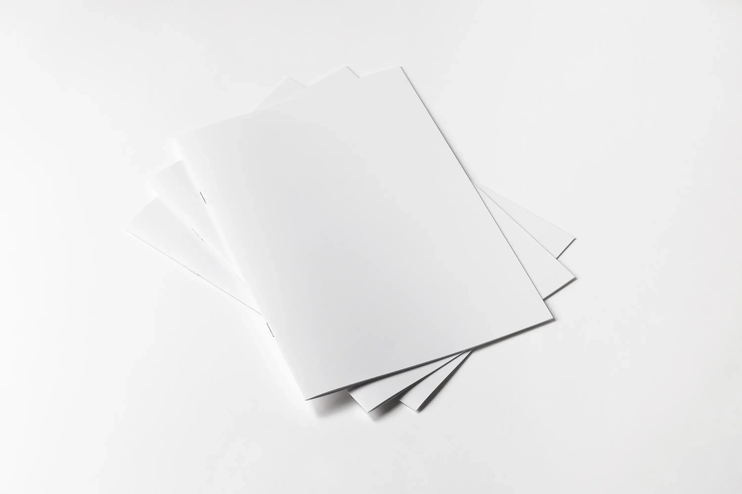Katalog szyty z miękką okładką ułożony na tle kilku egzemplarzy, prezentujący estetyczne zszycie oraz trwałe wykończenie publikacji.